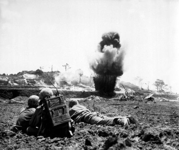 A demolition crew from the 6th Marine Division watches dynamite charges explode and destroy a Japanese cave. Okinawa, May 1945